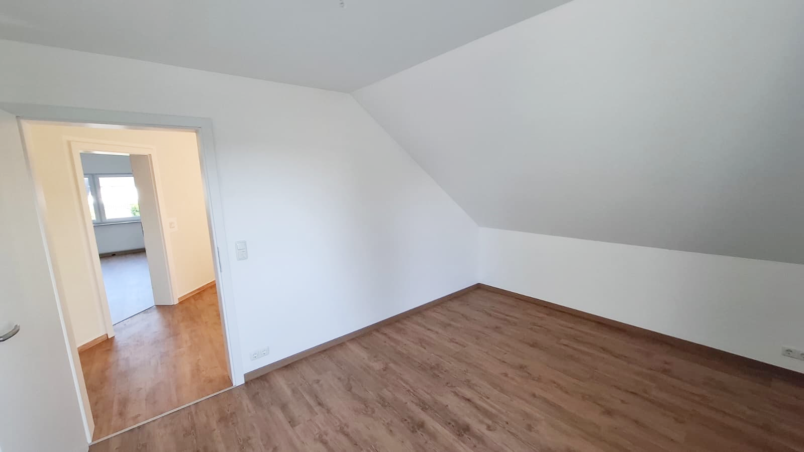 Helle Wand- und Deckenflächen mit Dachschräge, Holzboden und Durchgang zum Flur