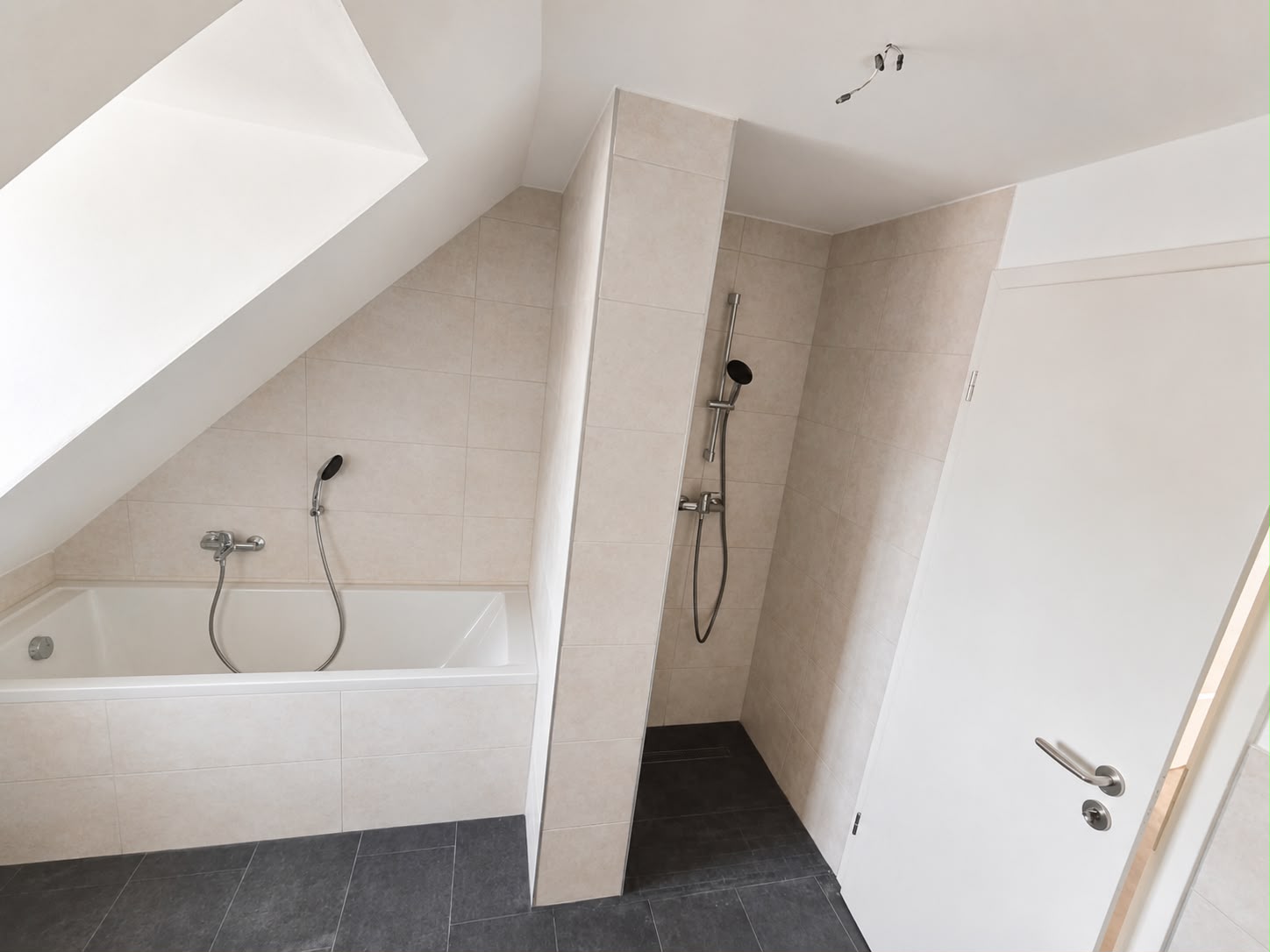 Helles Dachgeschossbad mit Badewanne, gefliester Duschtrennwand, weißer Tür und dunklen Bodenfliesen
