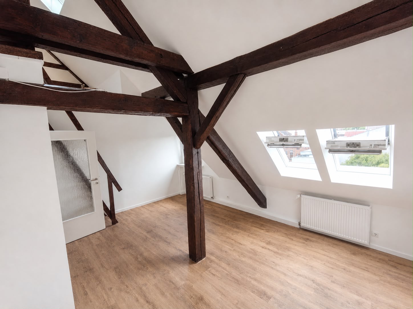 Dunkle Holzbalken und weiße Dachschrägen mit zwei Dachfenstern, Heizkörpern und Holzfußboden